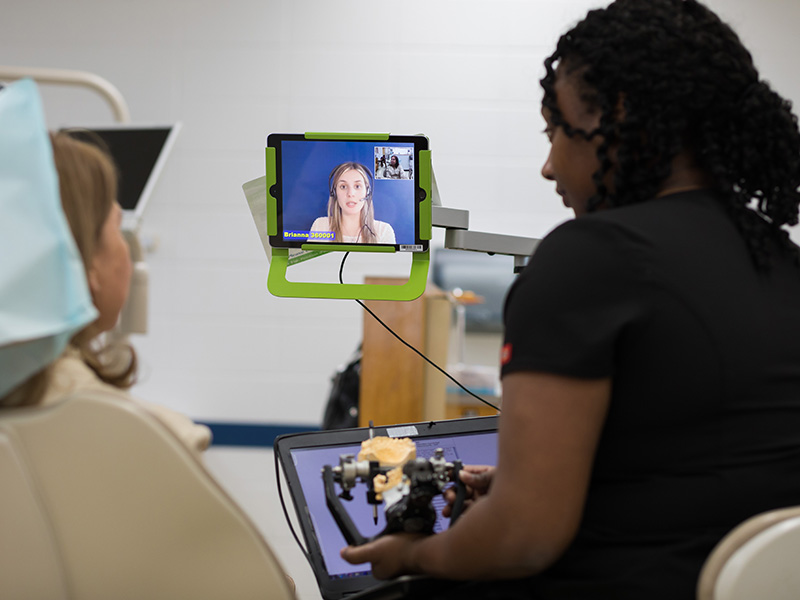 As School of Dentistry third-year student Kendra Clark, right, explains a dental procedure, a live video interpreter who speaks Portuguese prepares to translate Clark's English to patient and Brazil native Regina Wyatt.